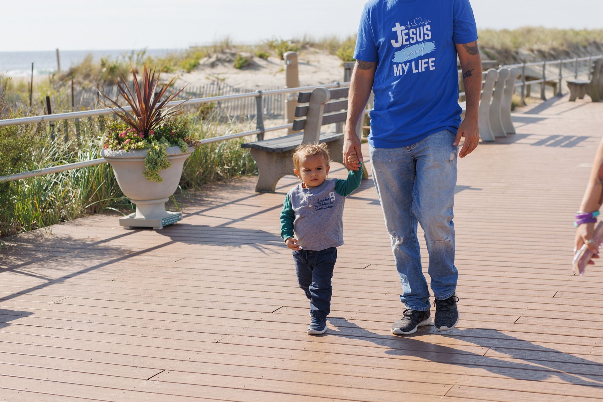 Man in blue shirt with child walking on boardwalk.