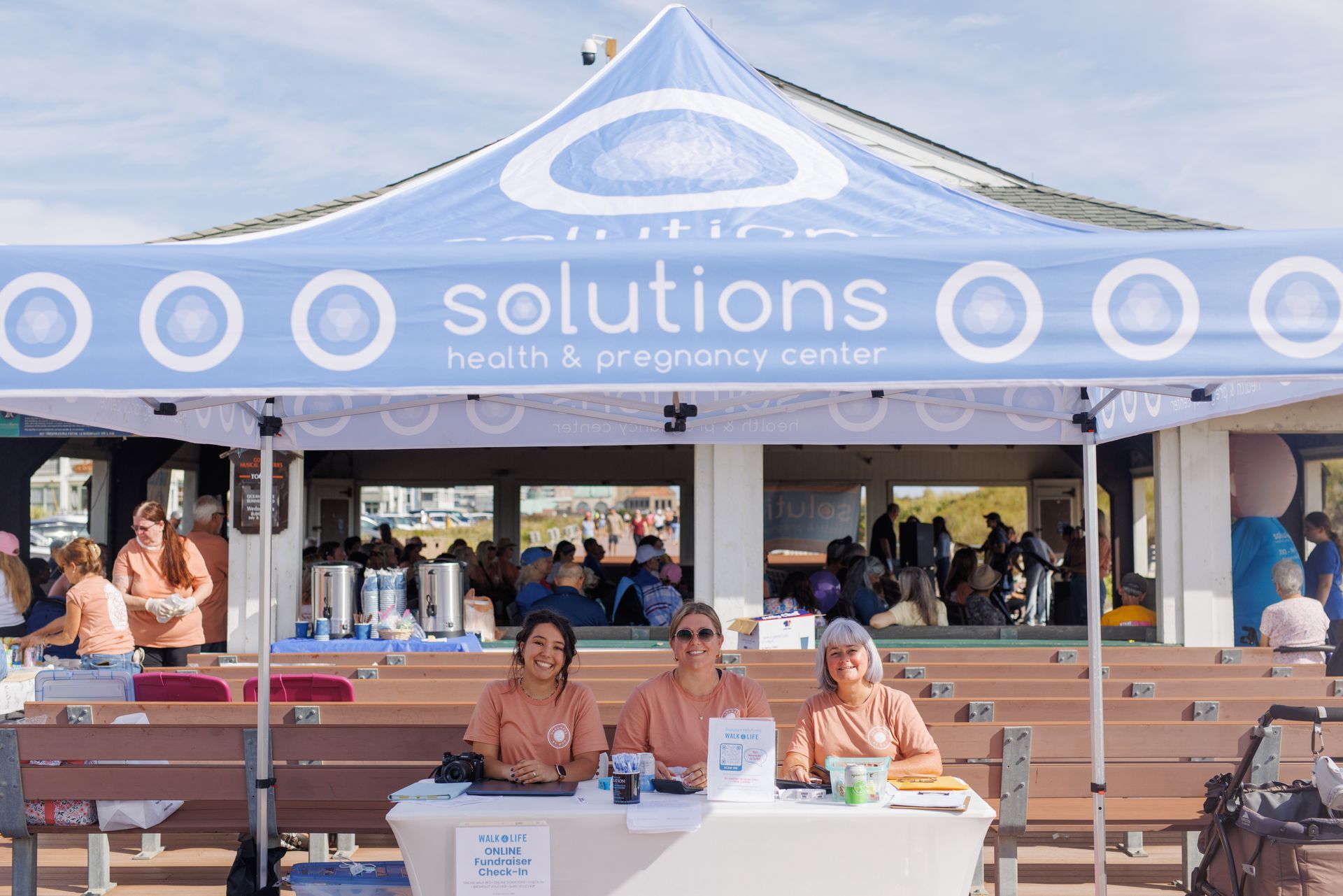 Three women at a Solutions Health & Pregnancy Center tent at an outdoor event.