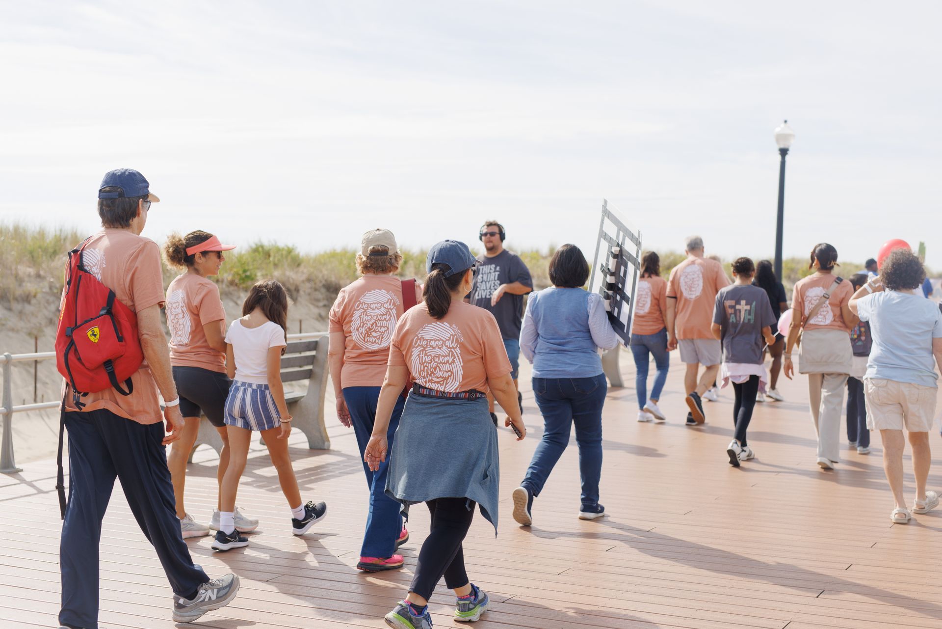 Group of people walking on a boardwalk, many wearing orange shirts with a design on the back.