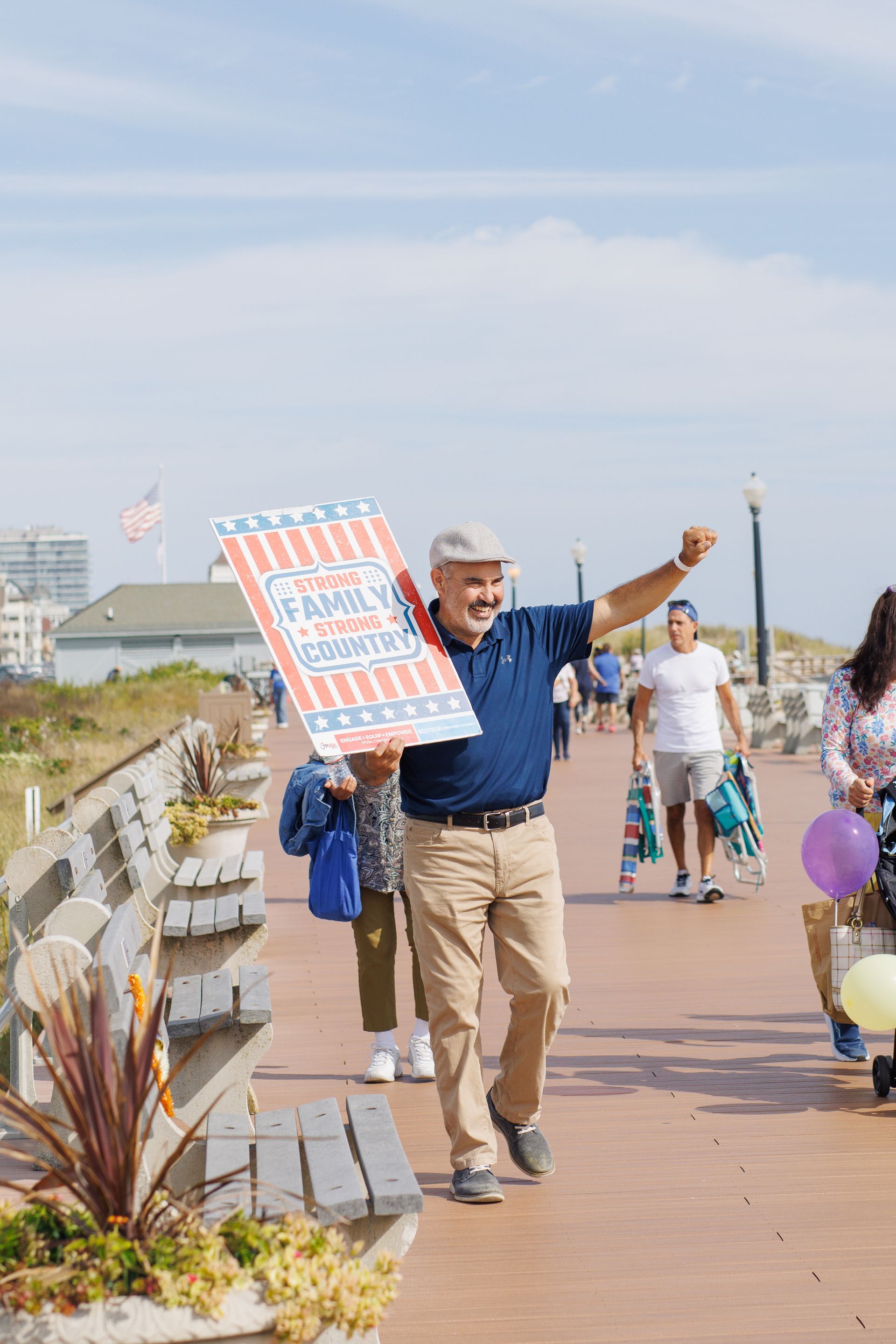 Man holding sign with American flag design on boardwalk, gesturing.