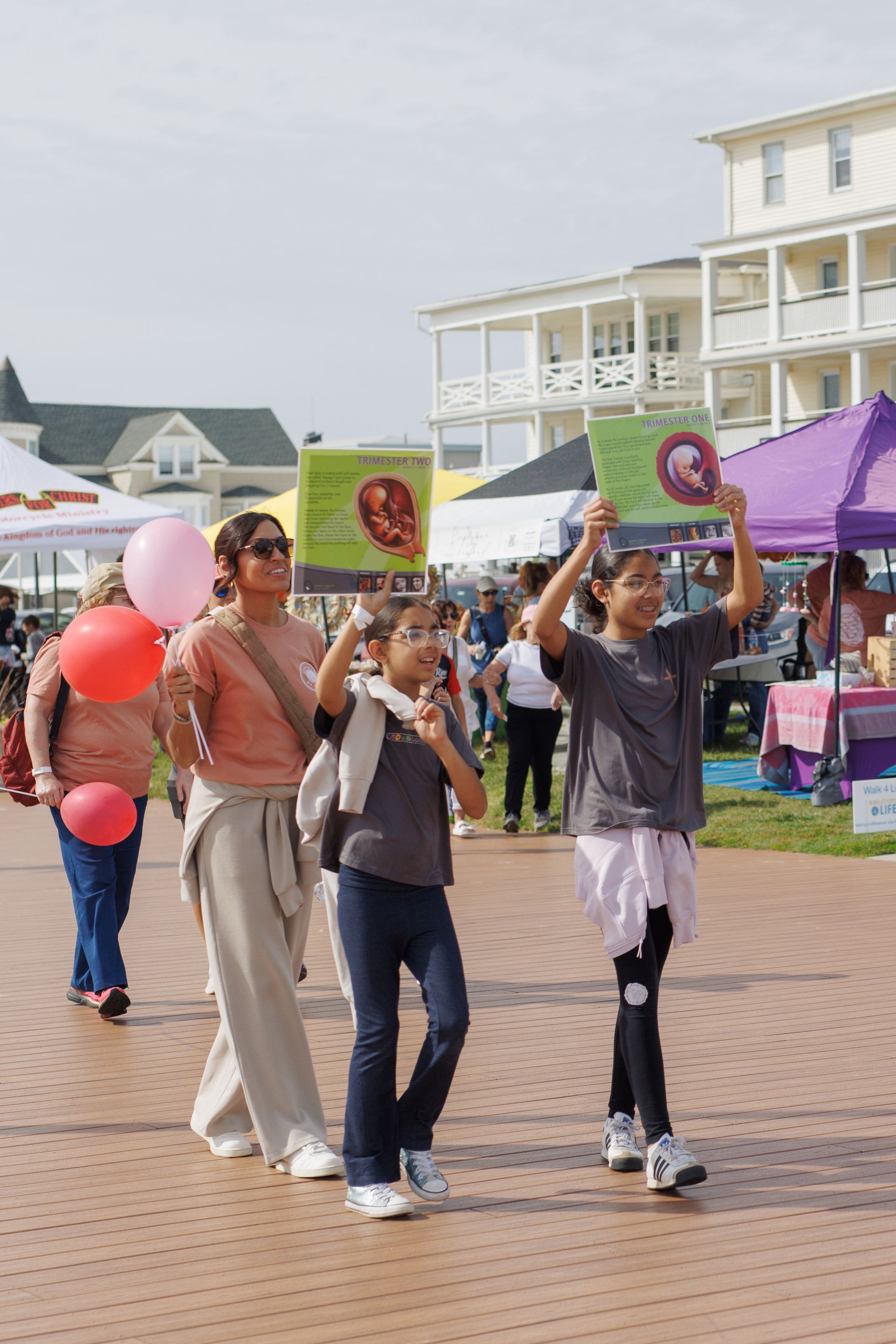 People walking with signs and balloons at an outdoor event near buildings.