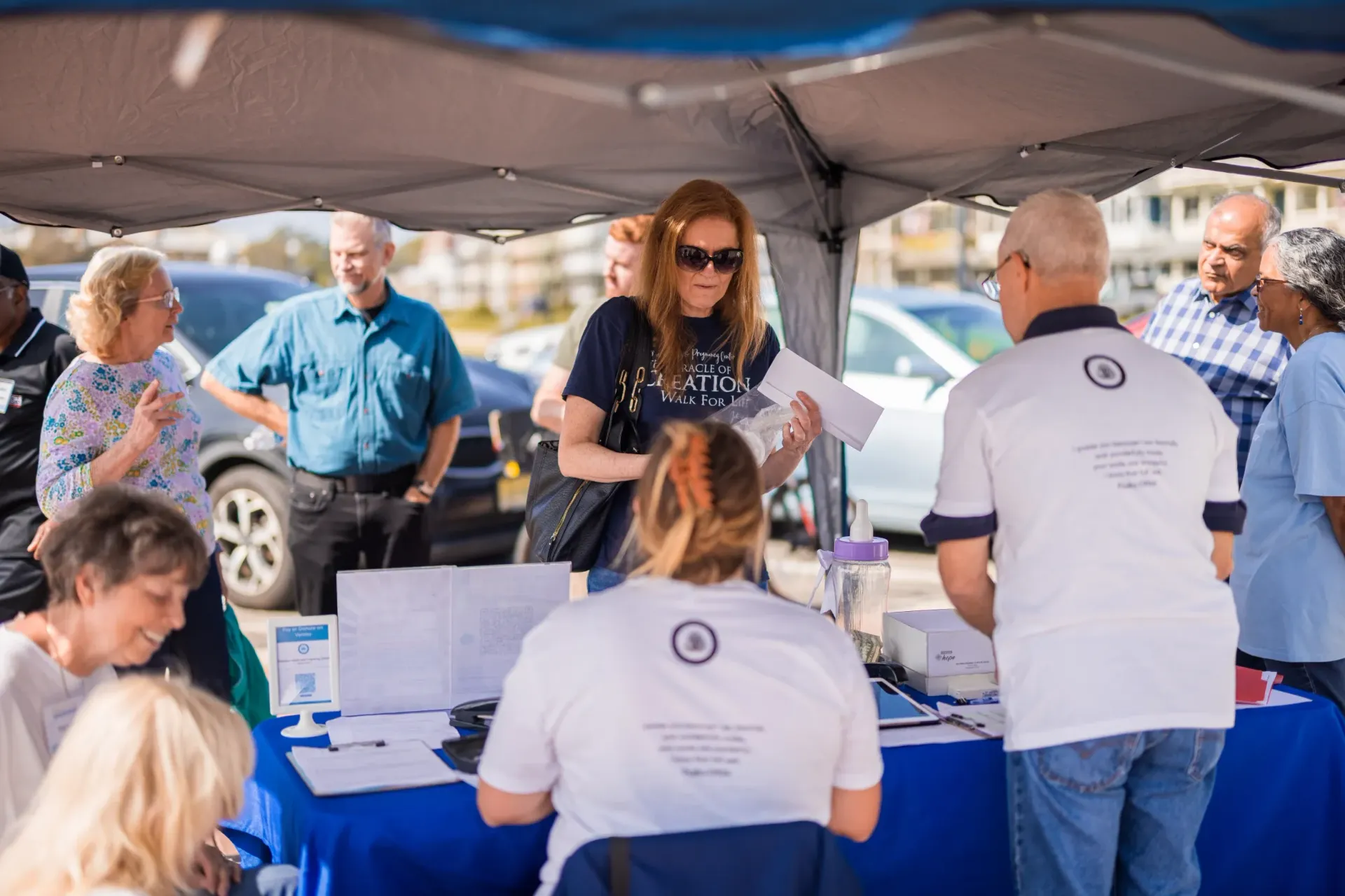 A group of people are standing around a table under a tent.