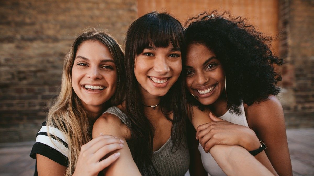 Three young women are posing for a picture together and smiling.