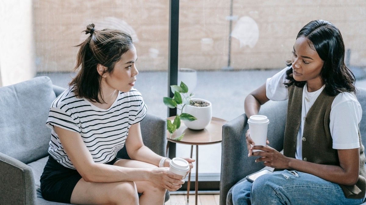 Two women are sitting on a couch talking to each other.