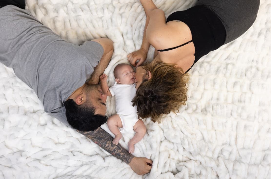 A man and a woman are laying on a bed with a baby.