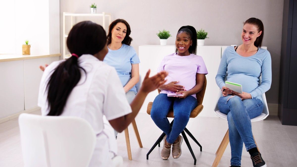 A group of pregnant women are sitting in a circle talking to a nurse.