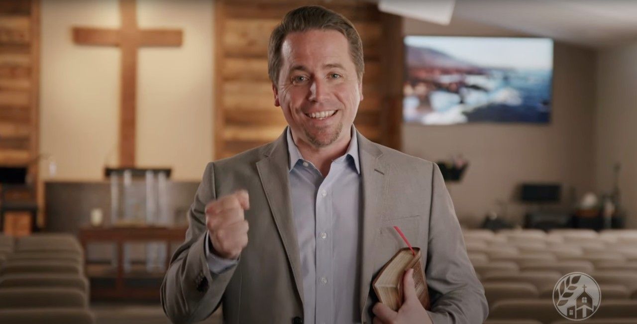 A man in a suit is holding a bible in front of a coffin.