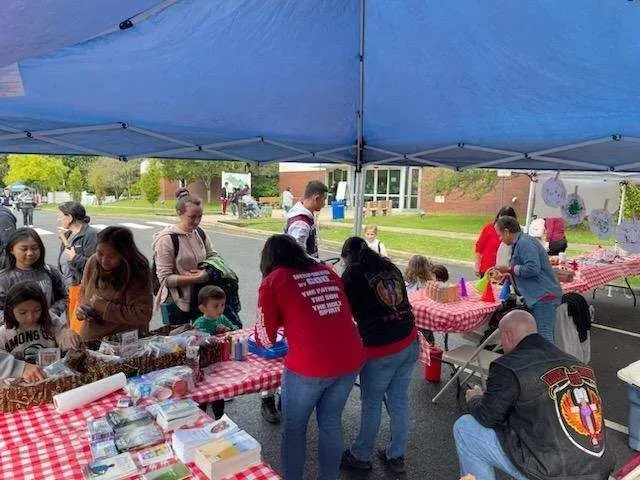 A group of people are standing around tables under a blue tent.