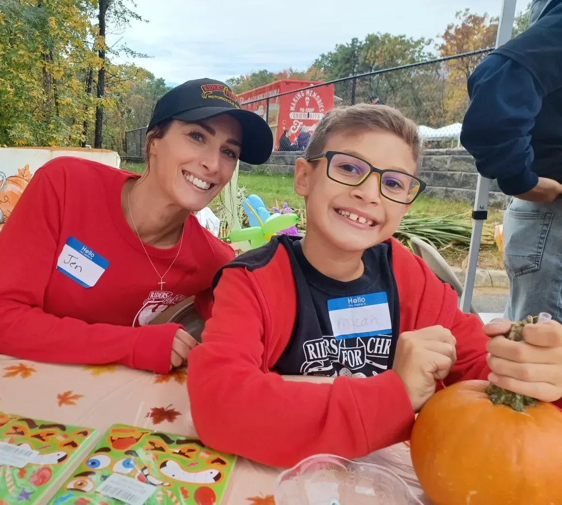 A woman and a boy are sitting at a table with a pumpkin.