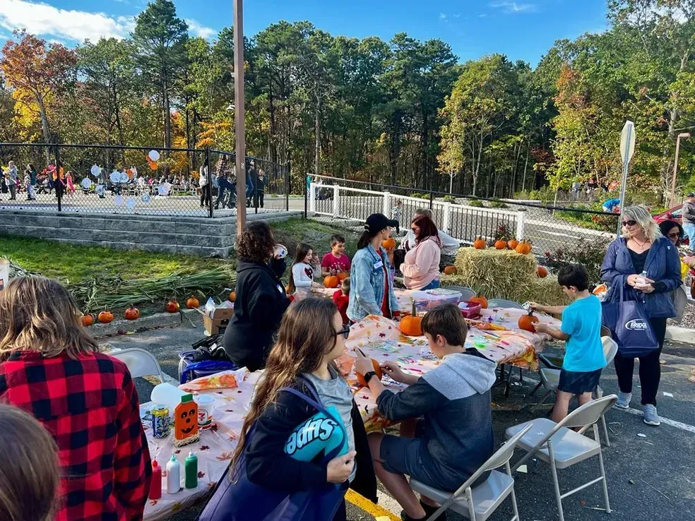 A group of people are sitting at tables in front of a pumpkin patch.