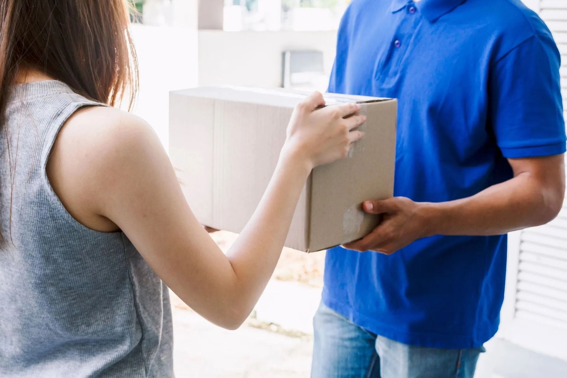 Dos personas intercambiando una caja de cartón en el interior de un edificio, una con una camisa azul.