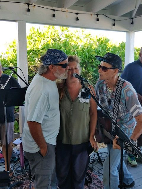 A woman singing into a microphone with two men standing behind her