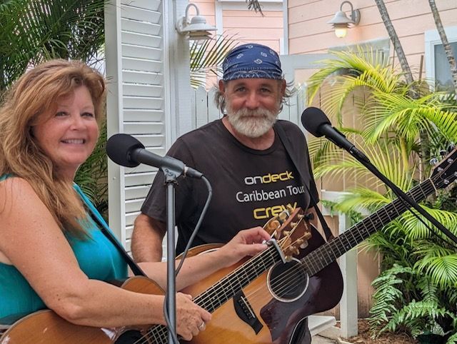 A man and a woman are playing guitars in front of microphones