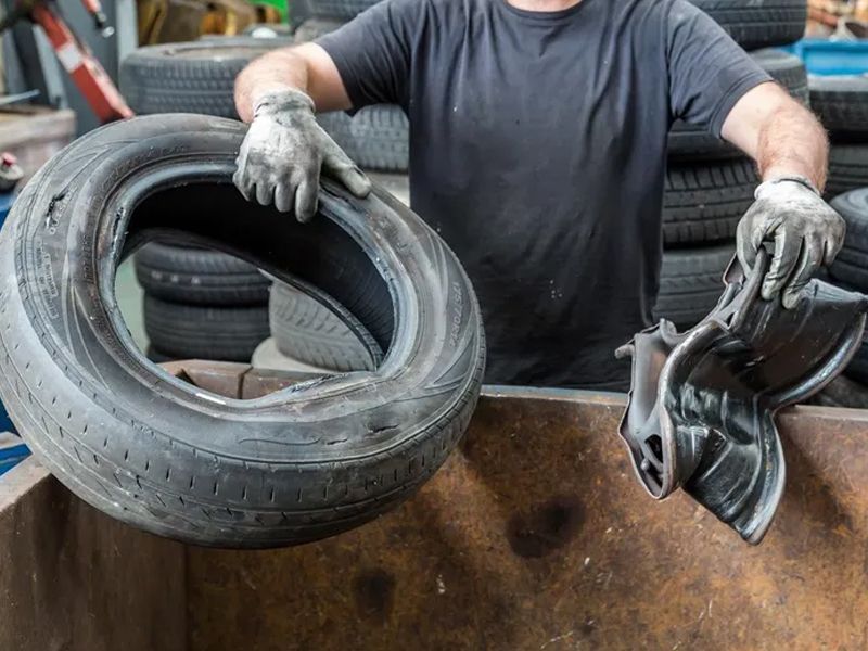 A man is holding a tire in his hands in front of a pile of tires.