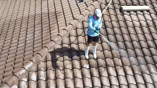 Person on a roof pressure washing. Blue sky background.