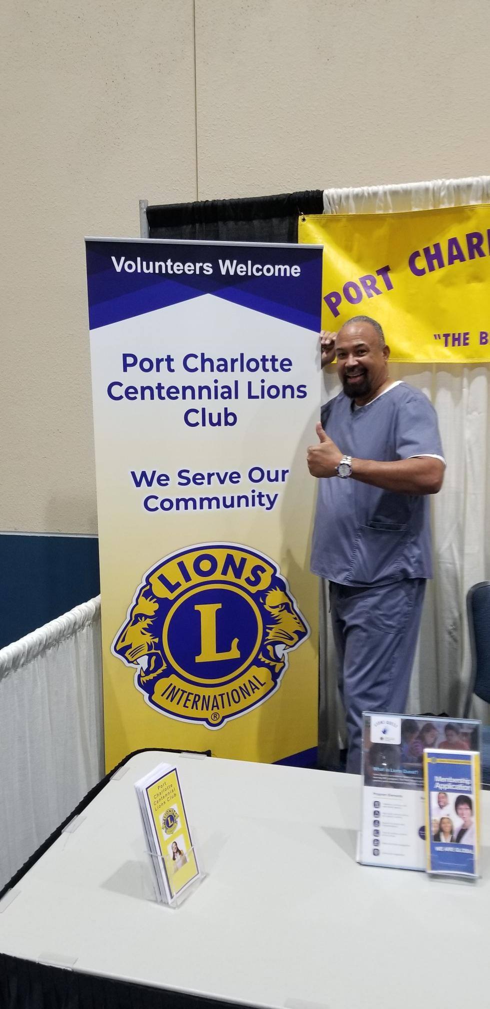 A man is standing in front of a sign for the port charlotte centennial lions club.