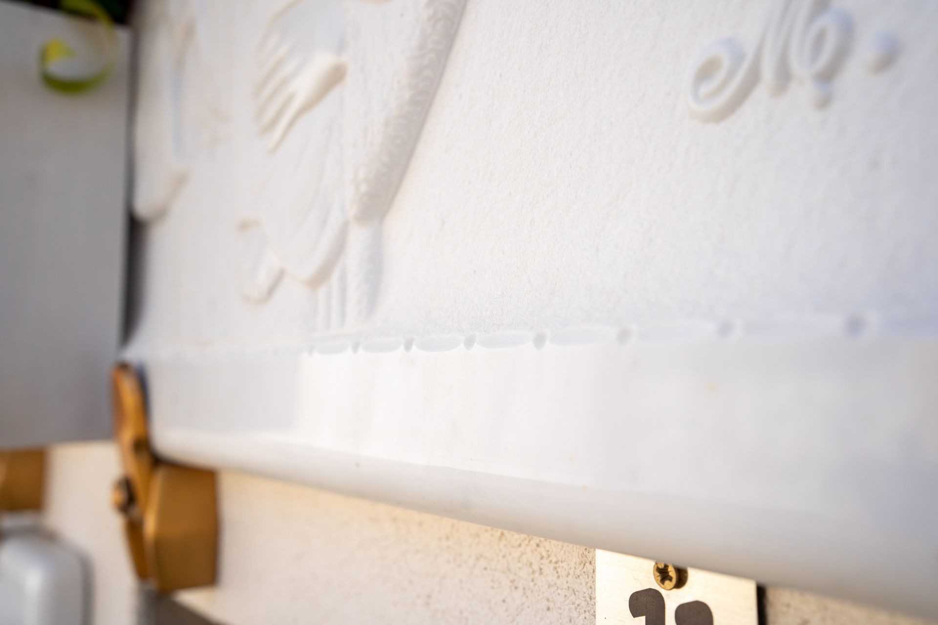 Primo piano di una tomba bianca con dettagli intagliati e ferramenta dorata, con una piccola targa sul fondo.