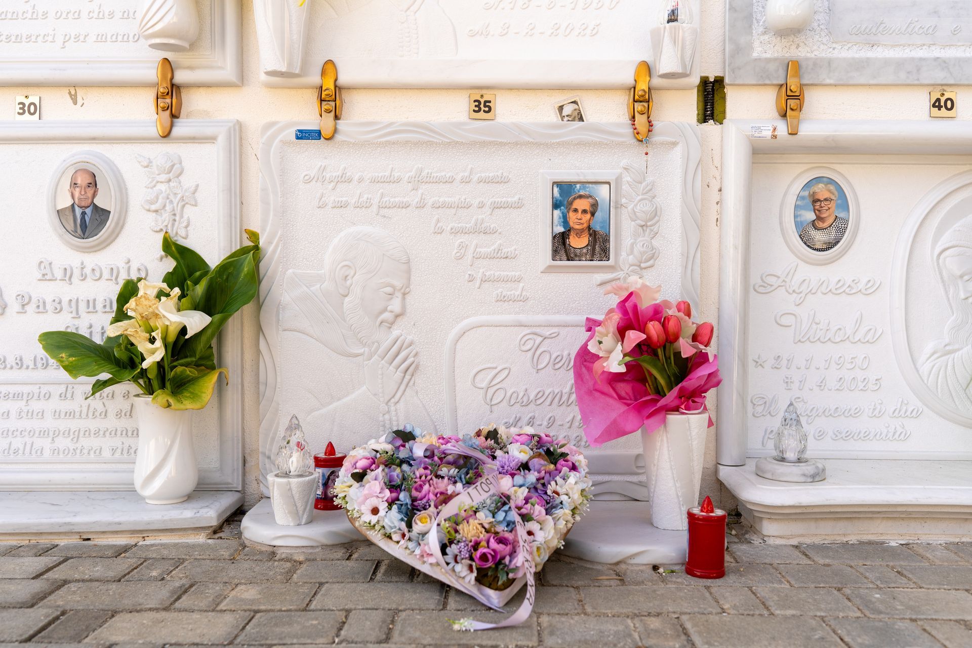 Tomba con ritratti, fiori e candele in un cimitero. Marmo bianco con dettagli dorati e bouquet.