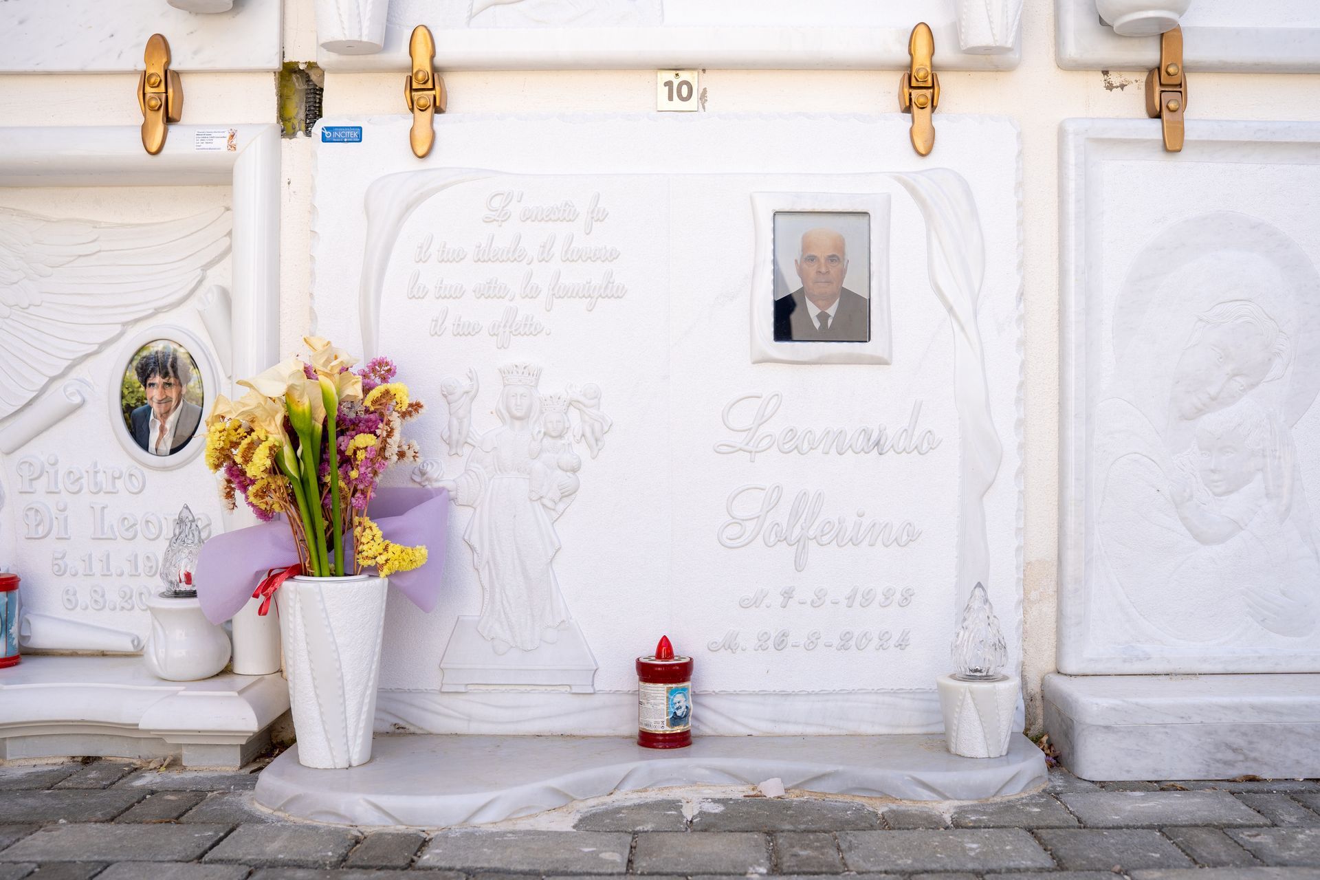 Tomba di marmo bianco con foto, fiori e testo in un cimitero.