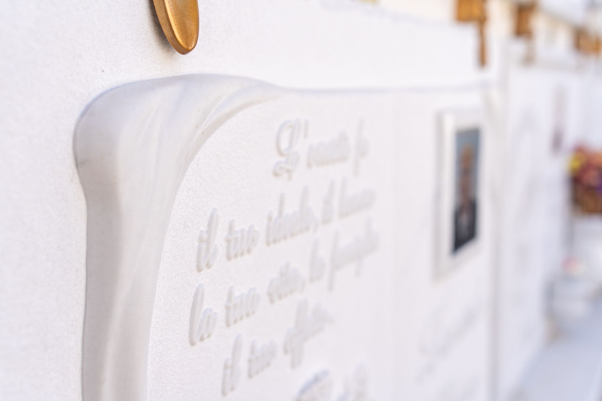 Tomba in marmo bianco con testo inciso e una piccola fotografia incorniciata.