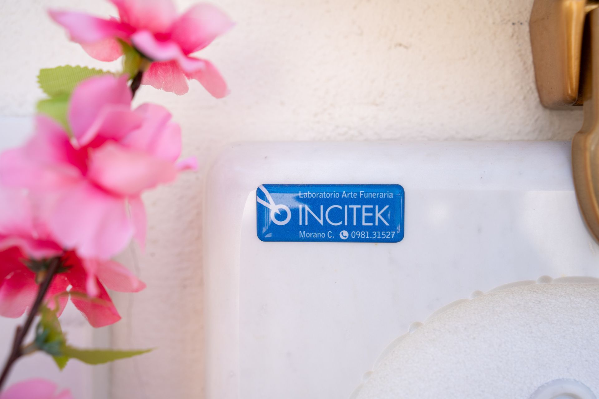 Fiori rosa accanto a una scatola bianca con un adesivo Incitek blu e una chiusura dorata.