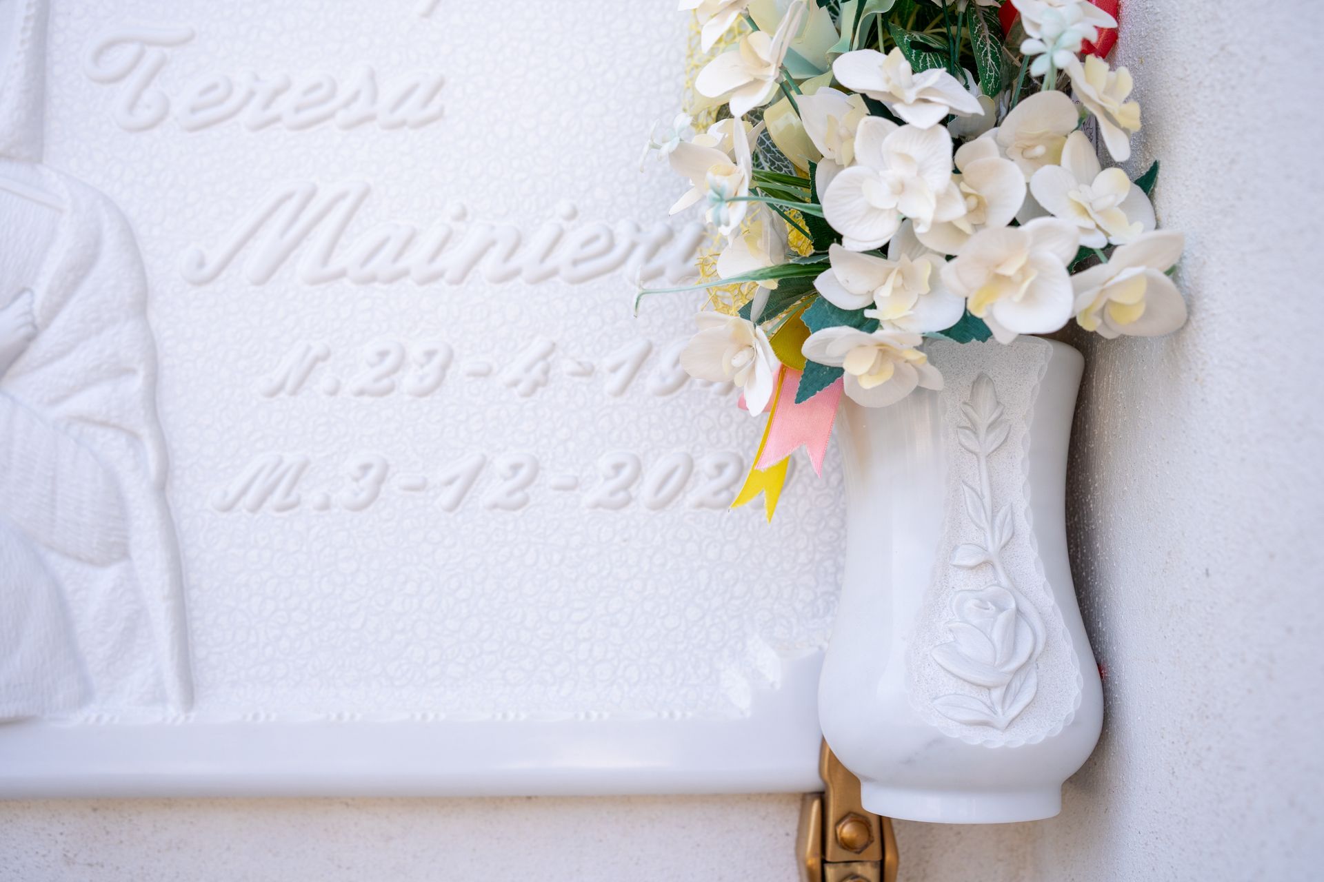 Lapide bianca con fiori in un vaso. Il testo riporta il nome 