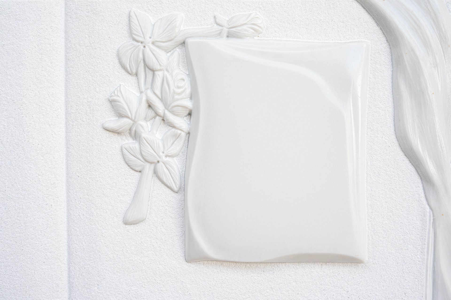 Una targa bianca con dei fiori sopra è su un muro bianco.