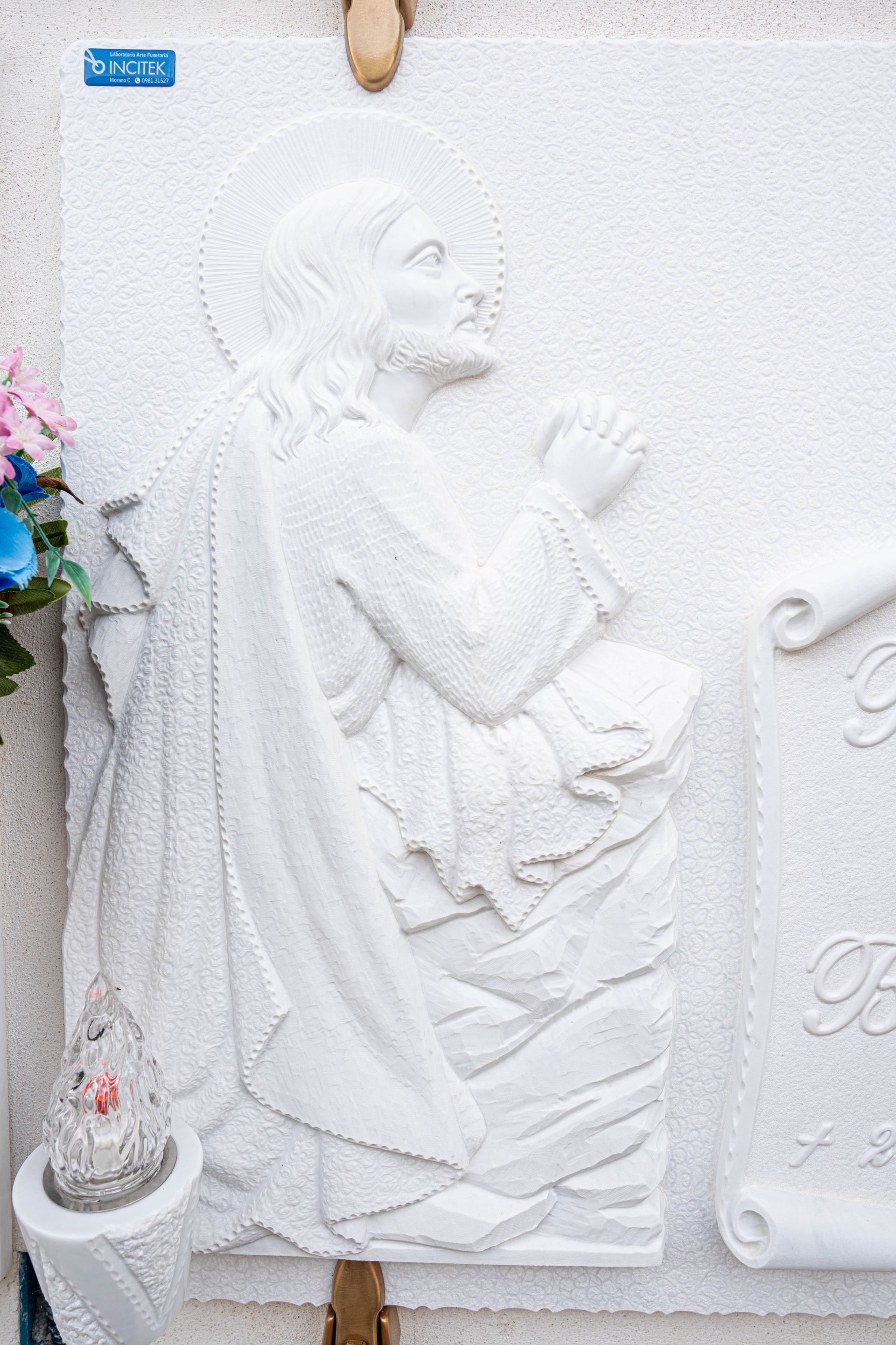 Una statua bianca di Gesù è su un muro accanto a un vaso di fiori.