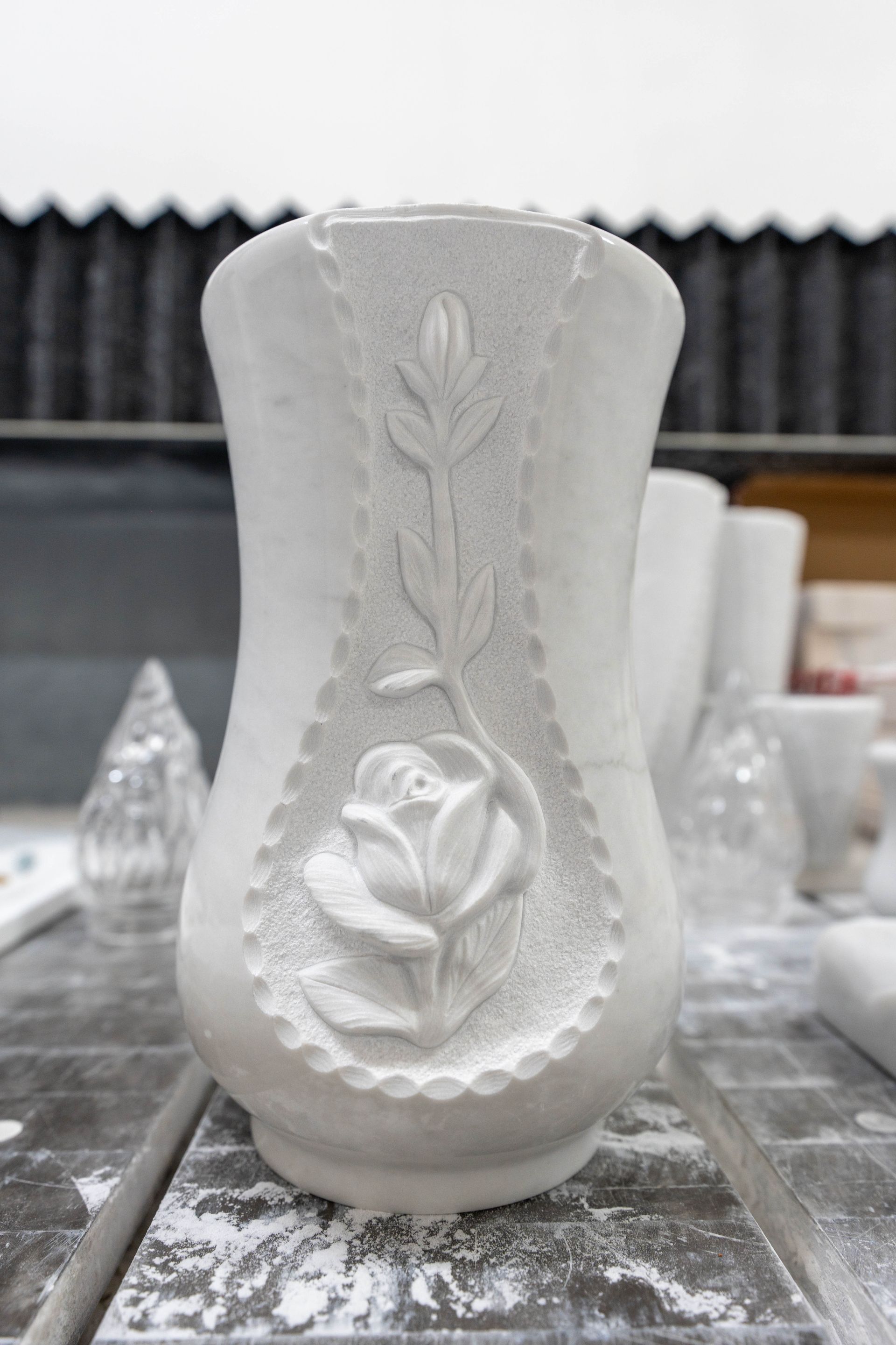 Su un tavolo c'è un vaso bianco con una rosa intagliata.