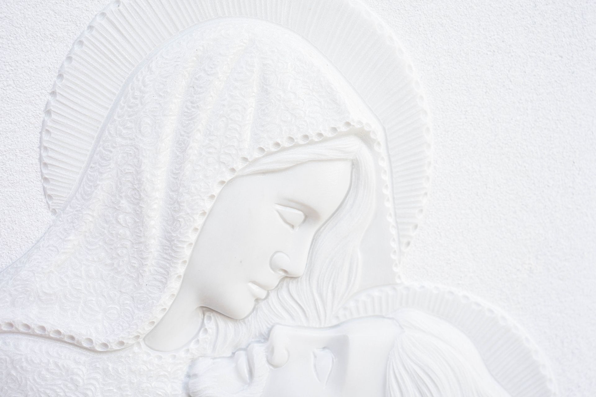 Un primo piano di una statua bianca di una donna che tiene in braccio un bambino.