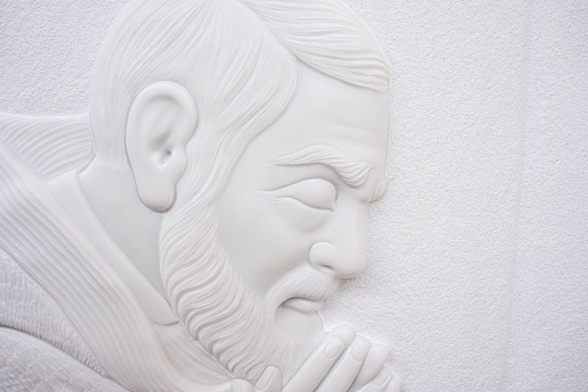Una statua bianca di un uomo con la barba sta pregando su un muro bianco.