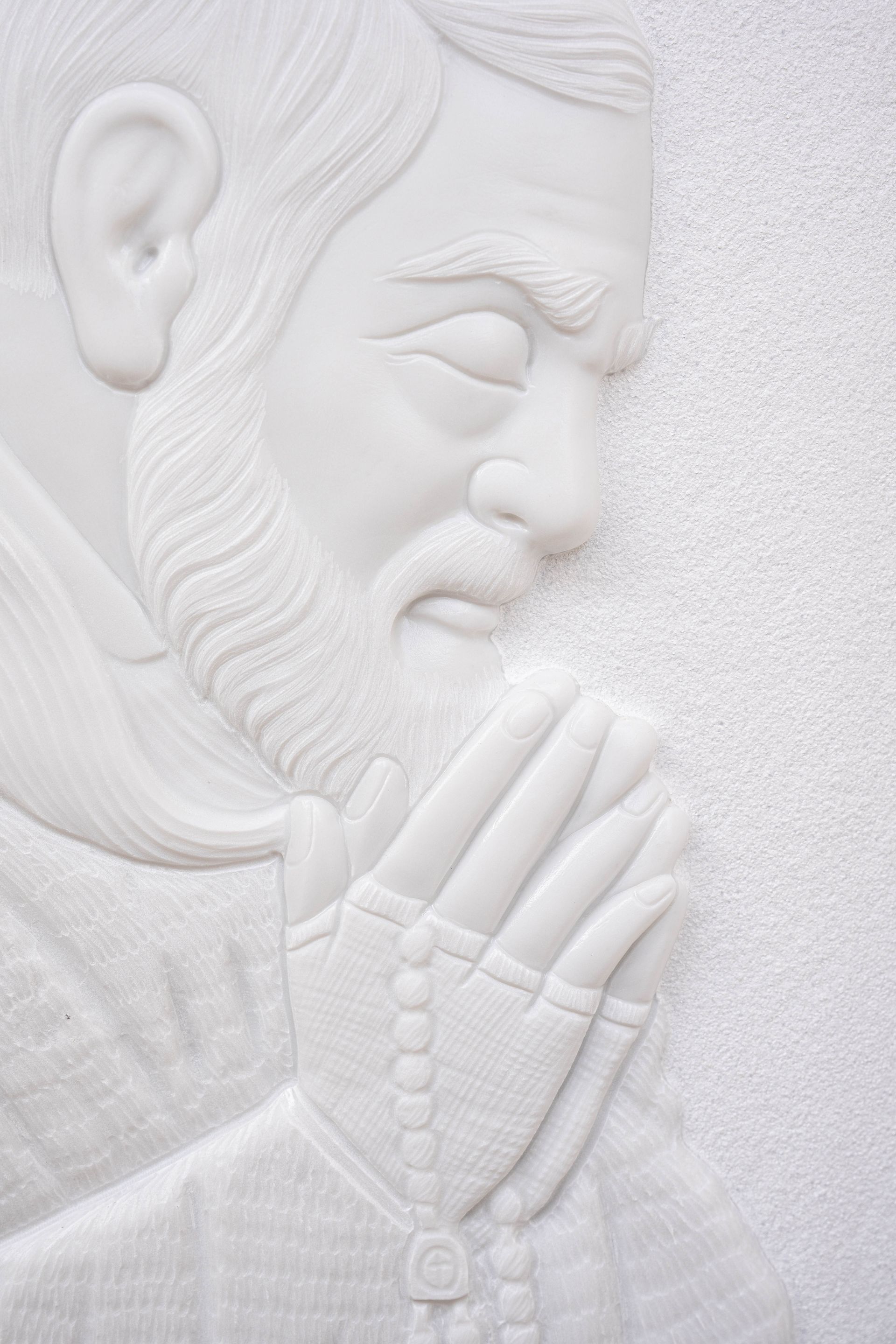 Una statua bianca di un uomo che prega con le mani giunte e un rosario.