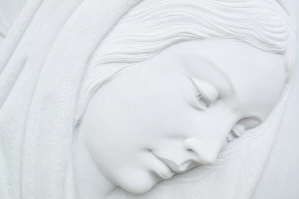 Un primo piano di una statua di una donna che dorme con gli occhi chiusi.