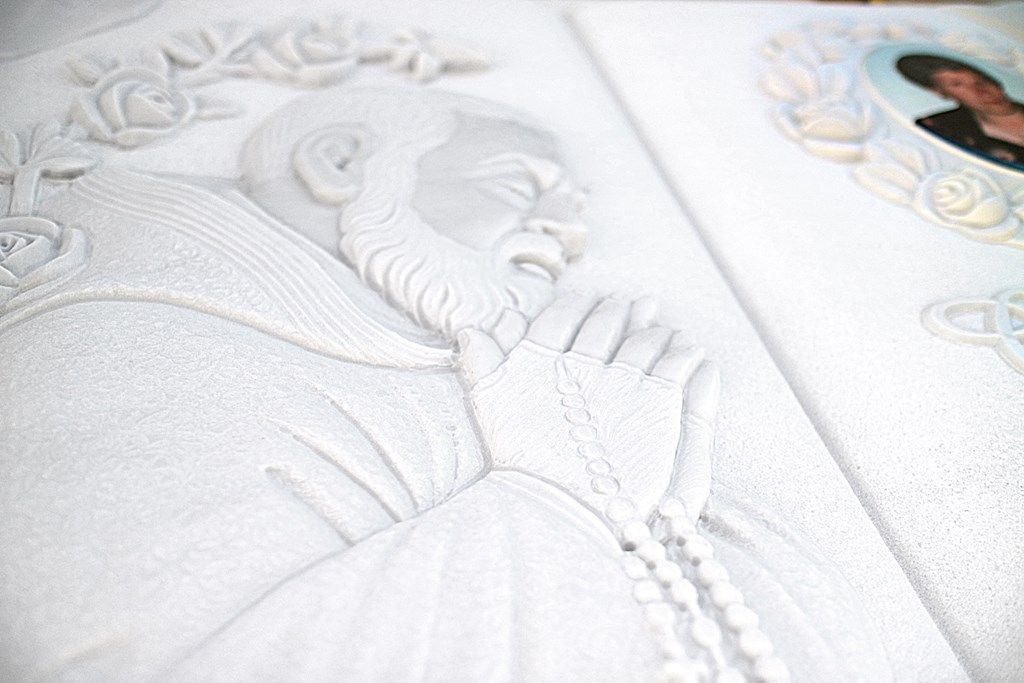 Una statua bianca di un uomo che prega con un rosario