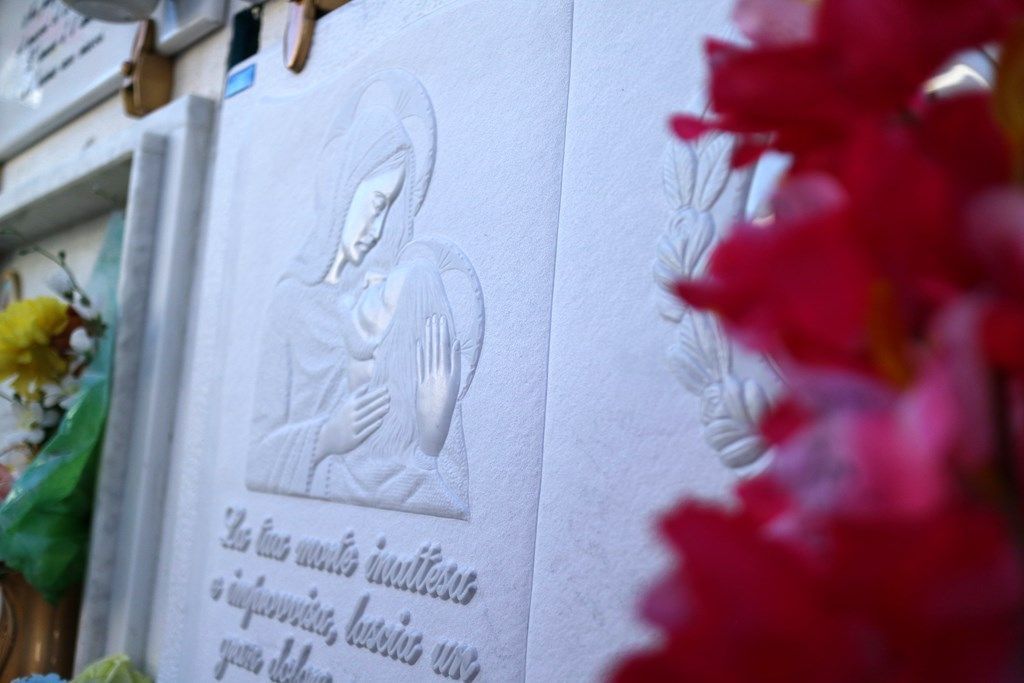 Una statua di una donna è su un muro con fiori in primo piano