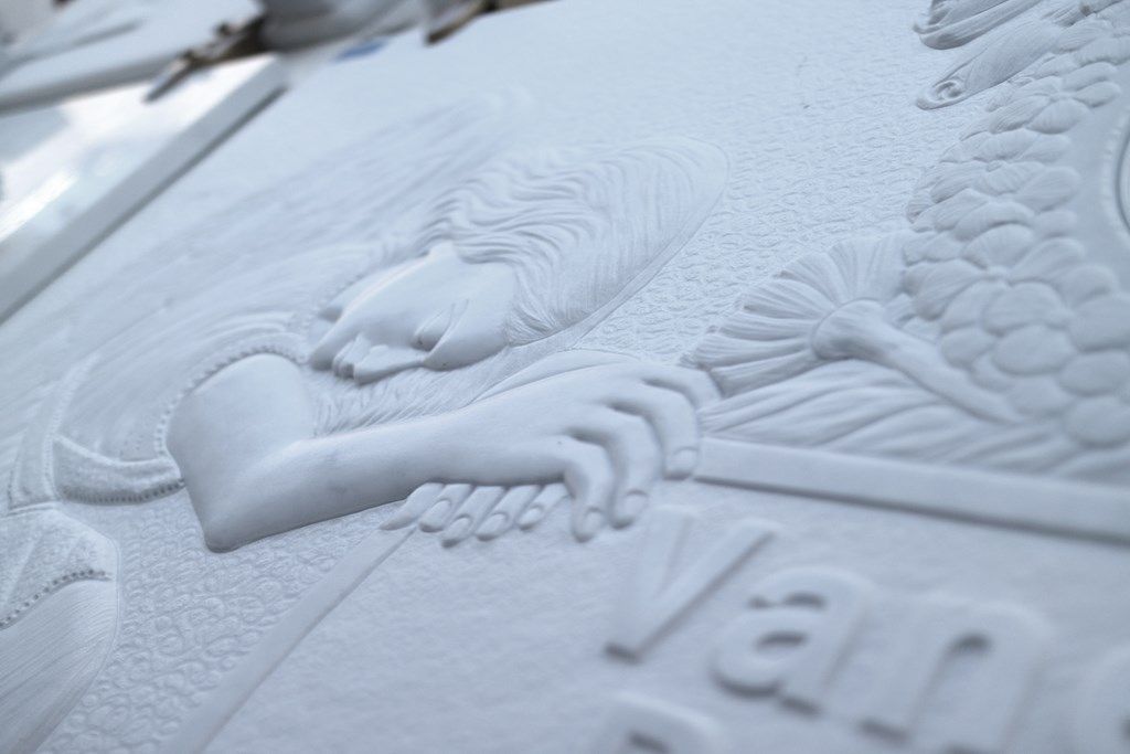 Una statua di una donna che tiene in mano un cuore è scolpita su una superficie bianca.