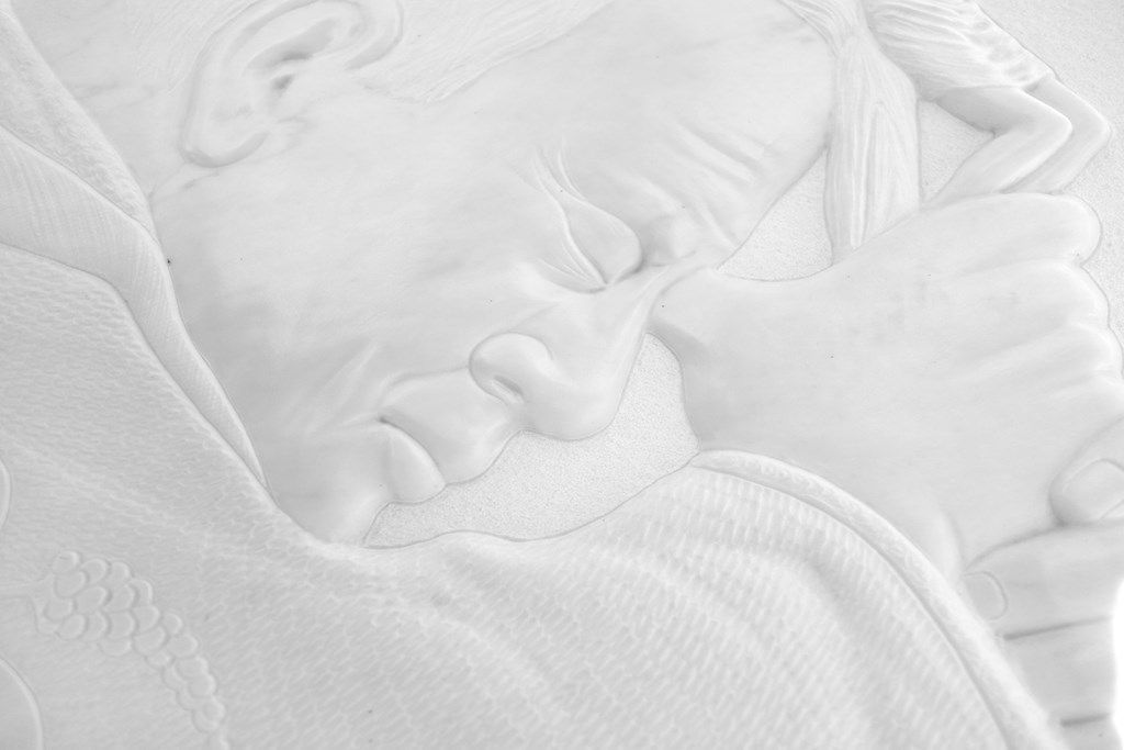 Un primo piano di una statua raffigurante un bambino che dorme su una coperta bianca.