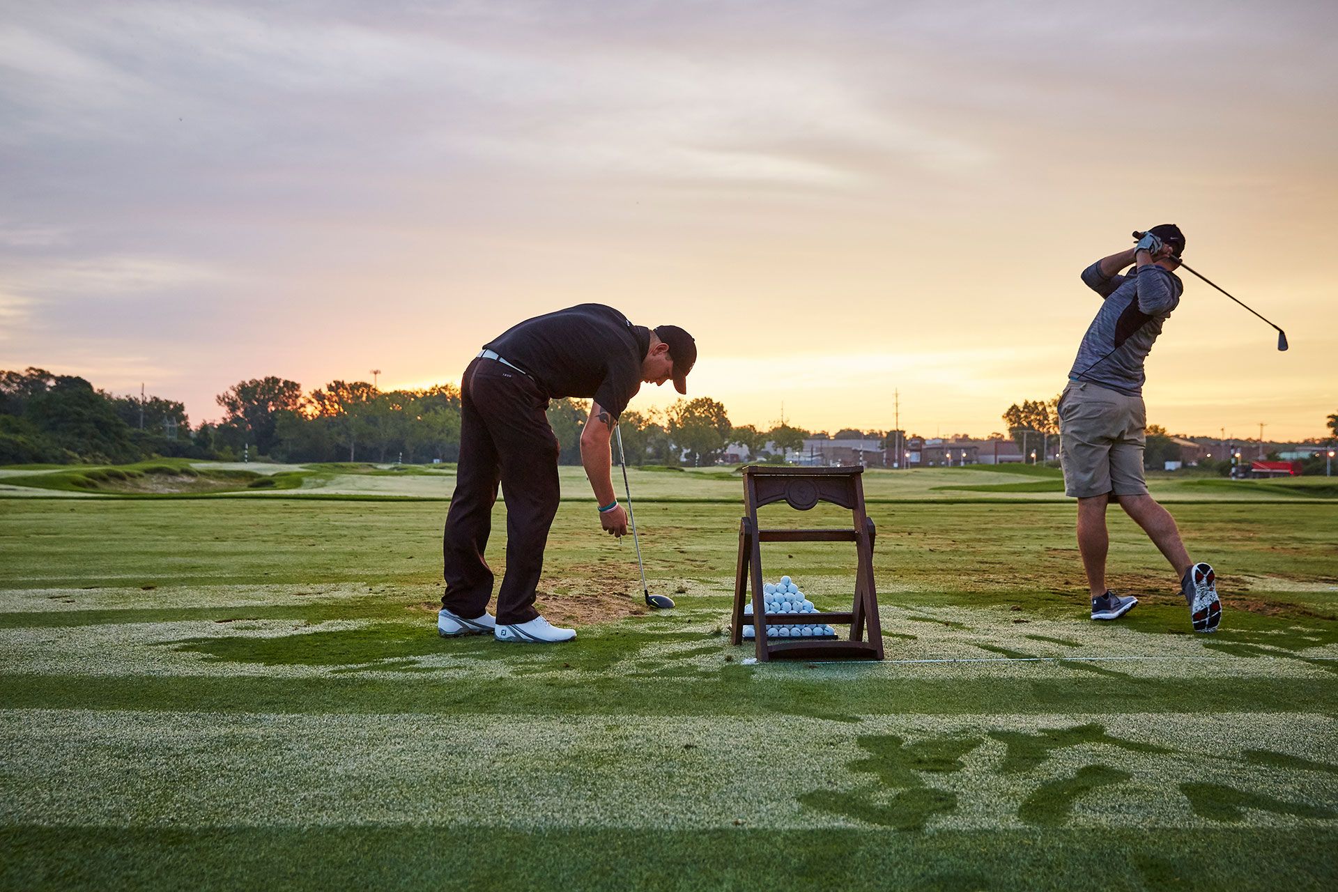 Two men are practicing golf on a golf course at sunset.