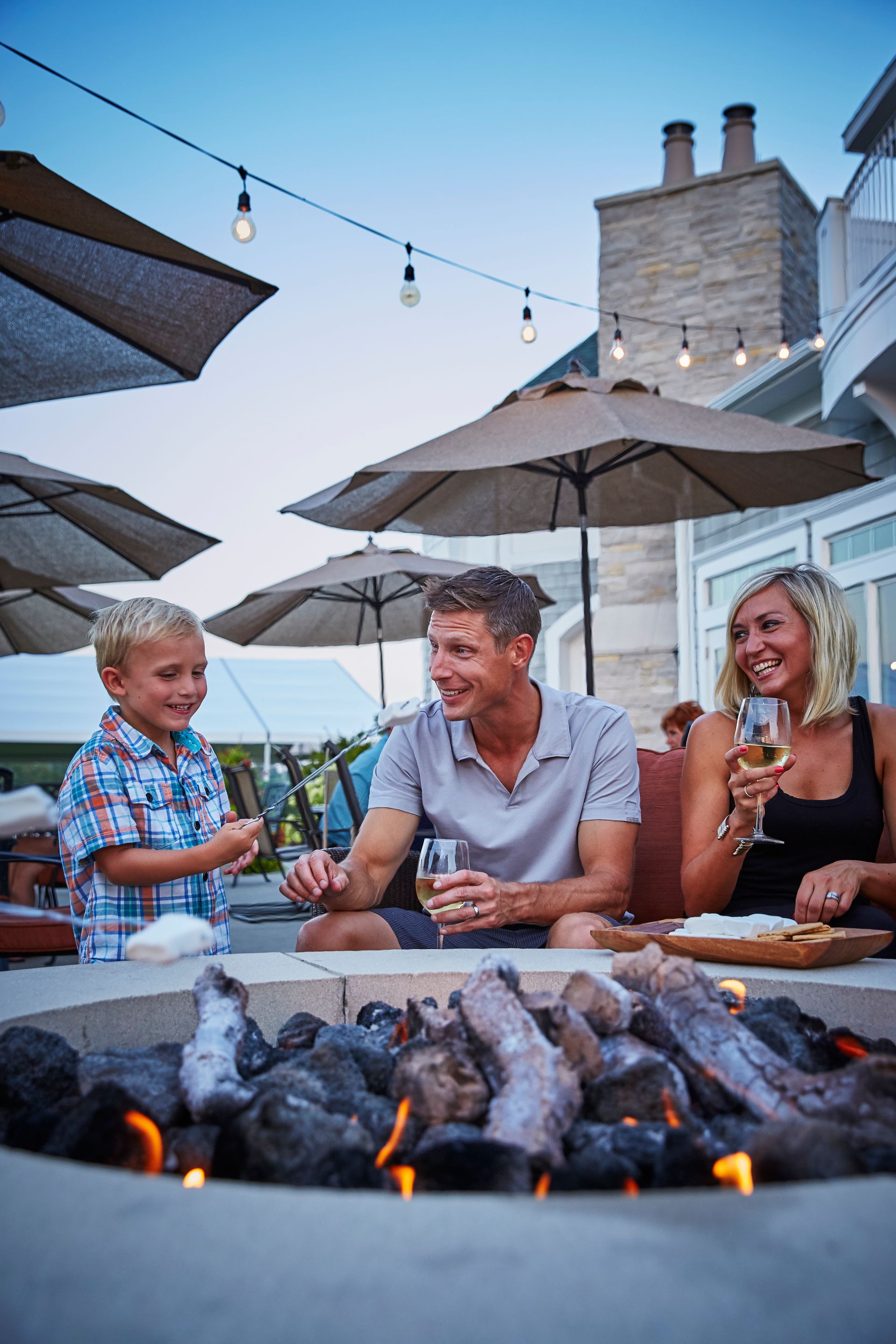 A family is sitting around a fire pit drinking wine.