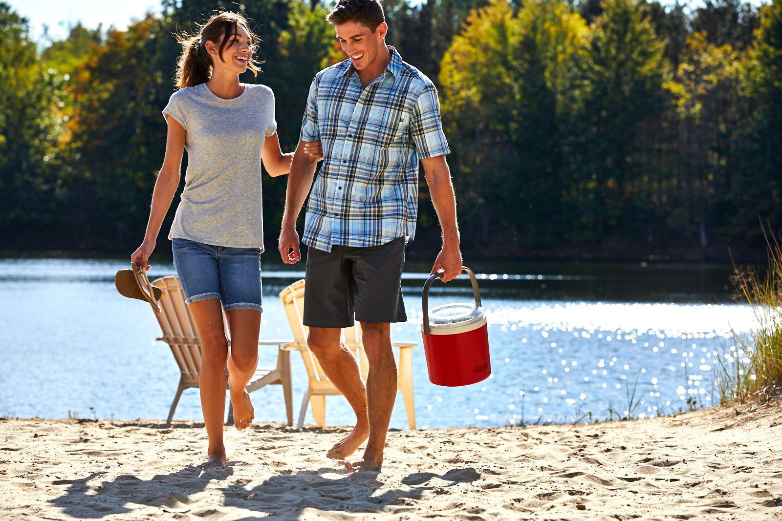 A man and a woman are walking on the beach near a lake.