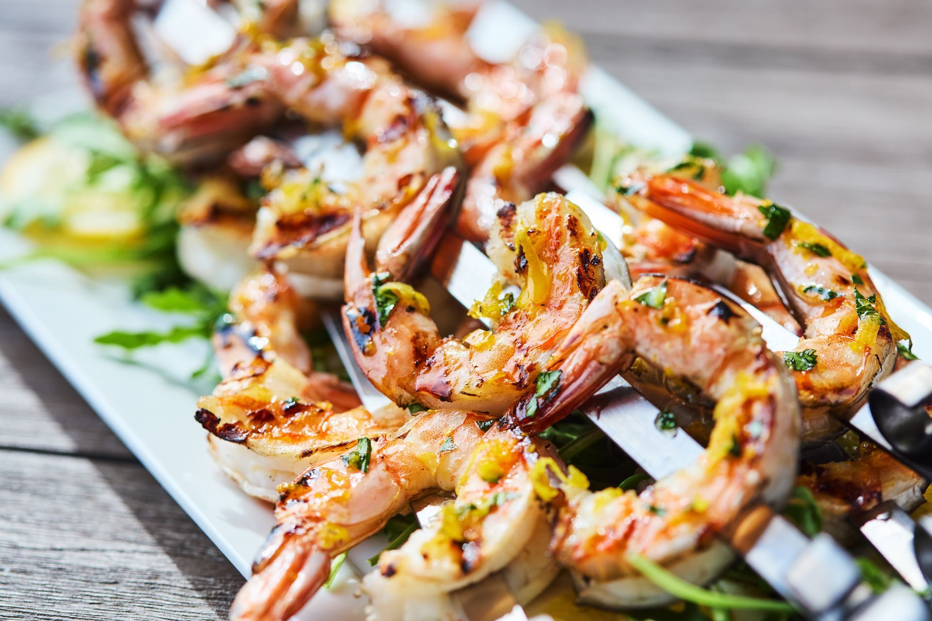 Grilled shrimp on skewers on a white plate on a wooden table.