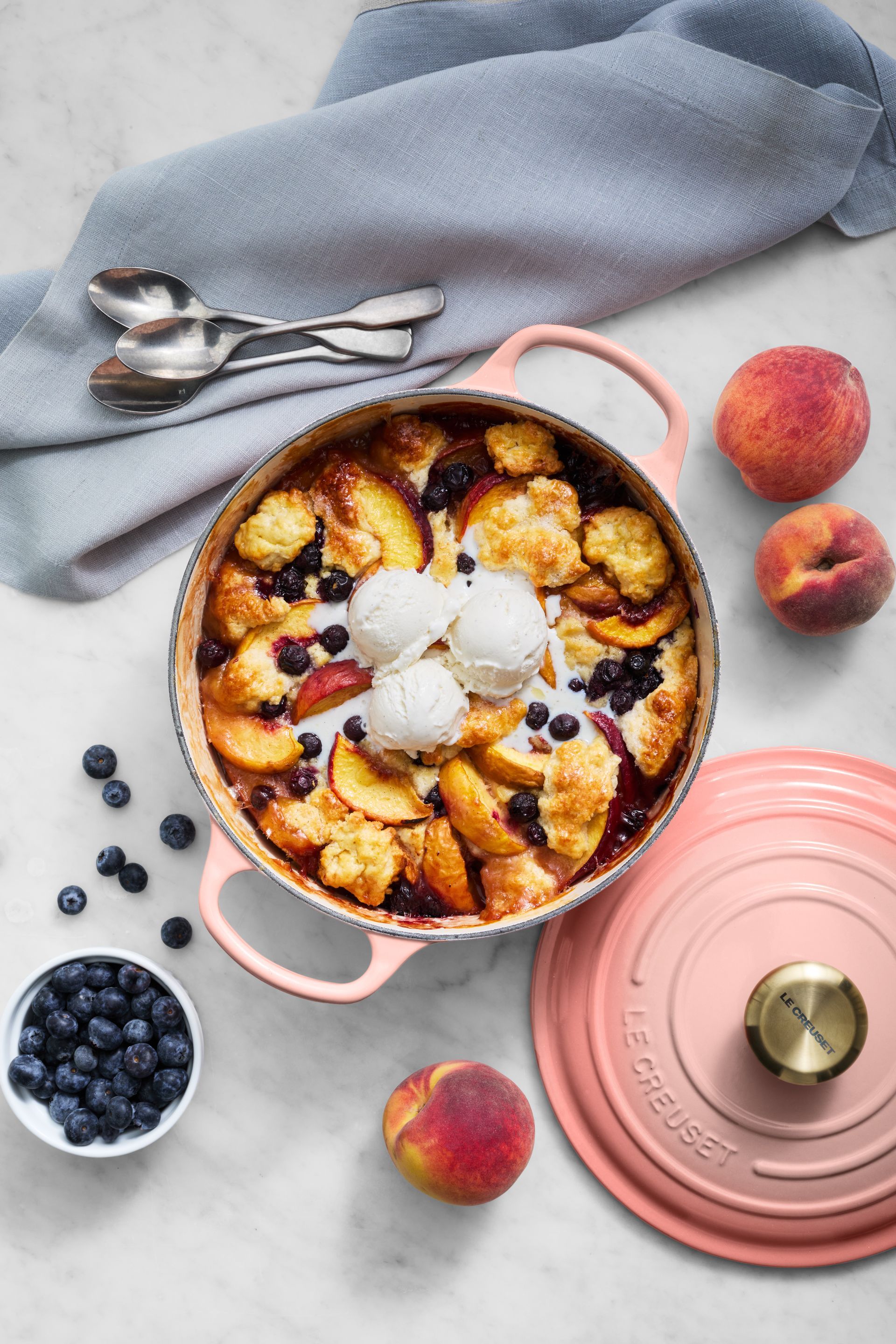 A pot of peach cobbler with ice cream and blueberries on a table.
