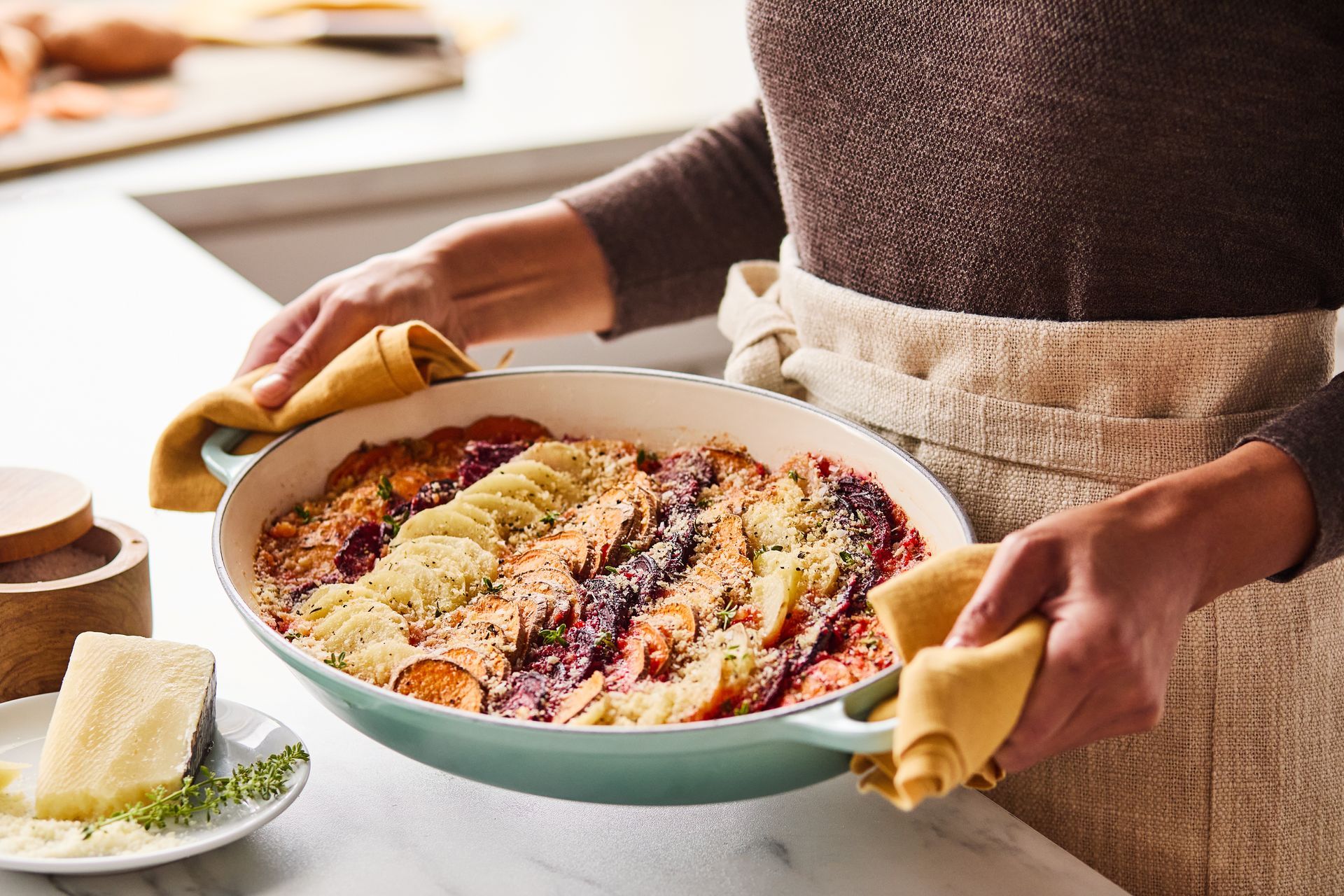 A woman is holding a Le Creuset pan with a beautiful casserole in in it.