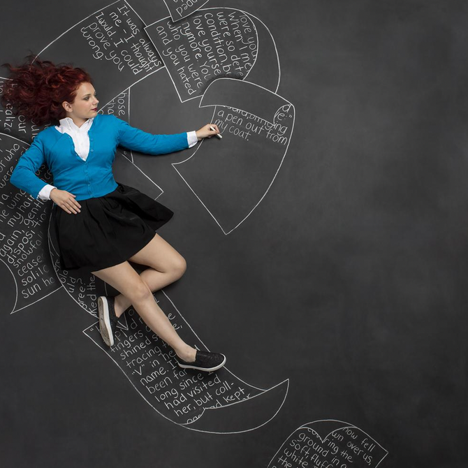 A woman in a blue sweater and black skirt is laying on a blackboard