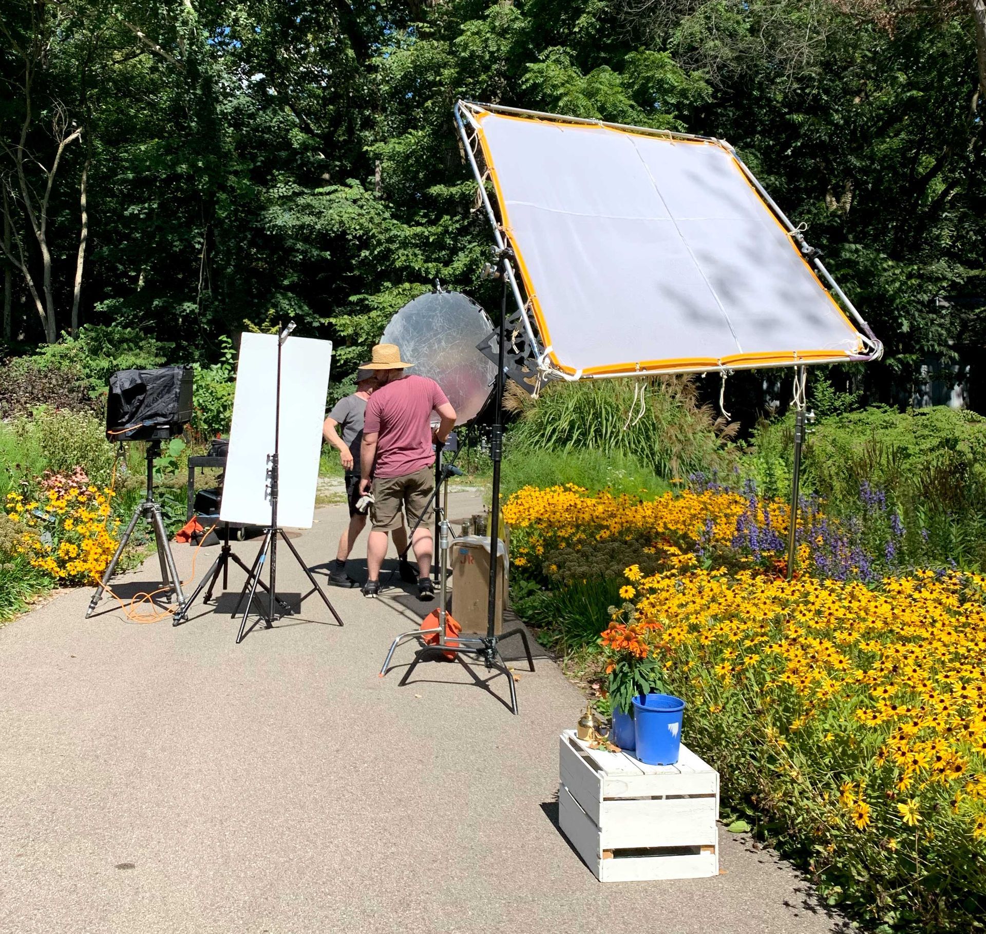 A man in a hat is walking down a path surrounded by flowers during a on location photoshoot.