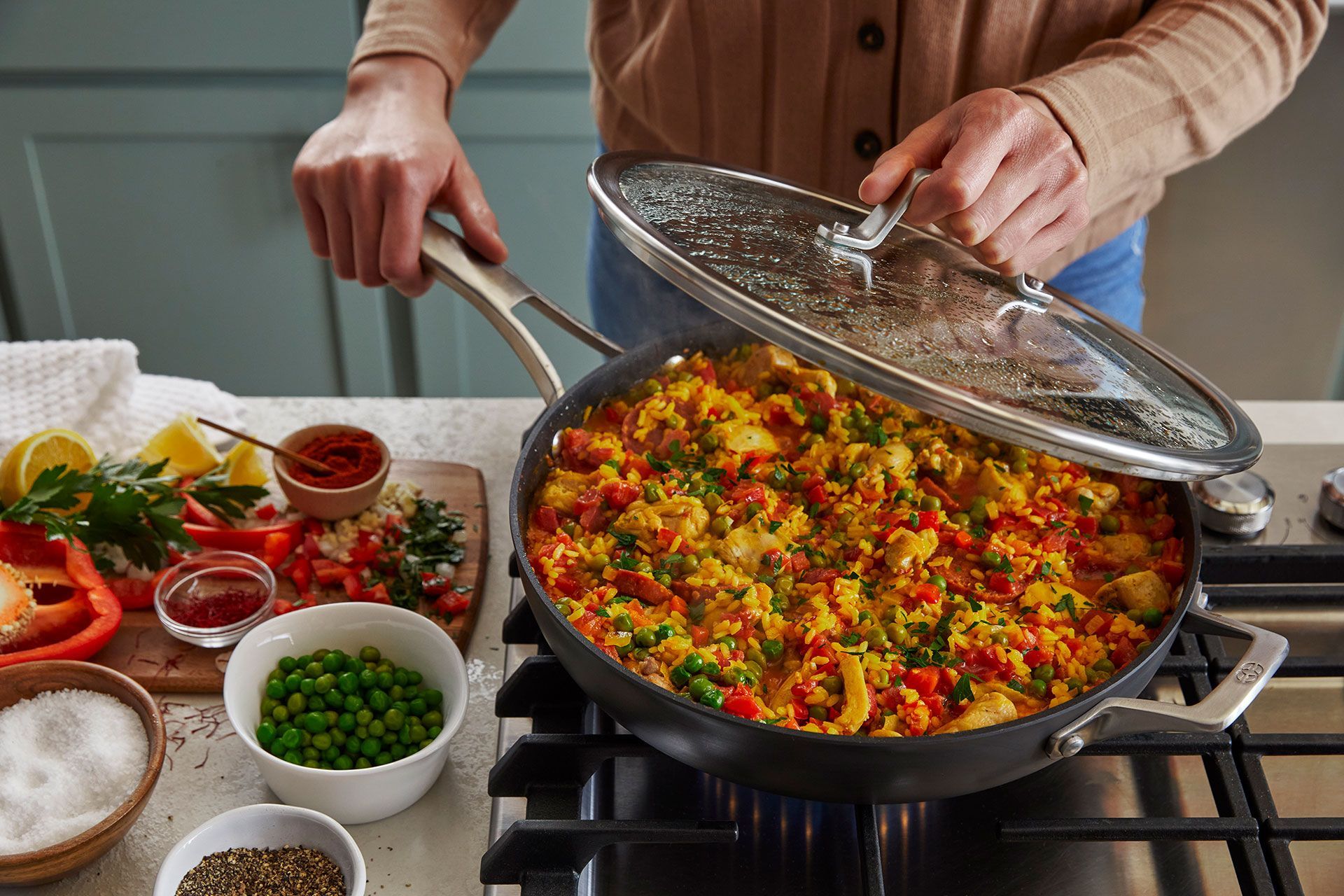 A person is cooking a paella in a pan on a stove with a Calphalon pan