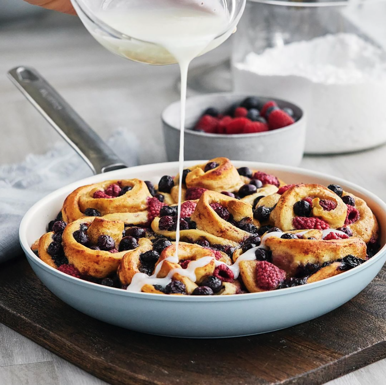 A person is pouring icing on a pan of fruit filled cinnamon rolls