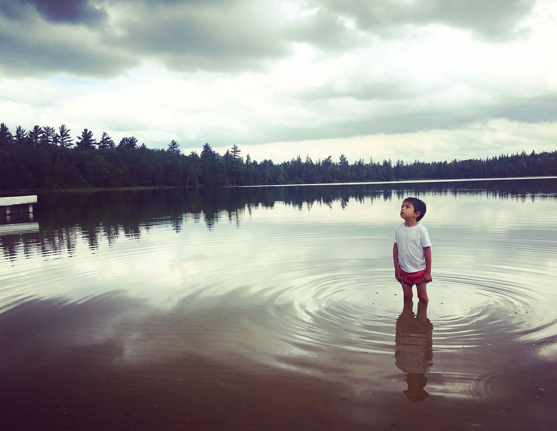 A young boy is standing in the middle of a lake