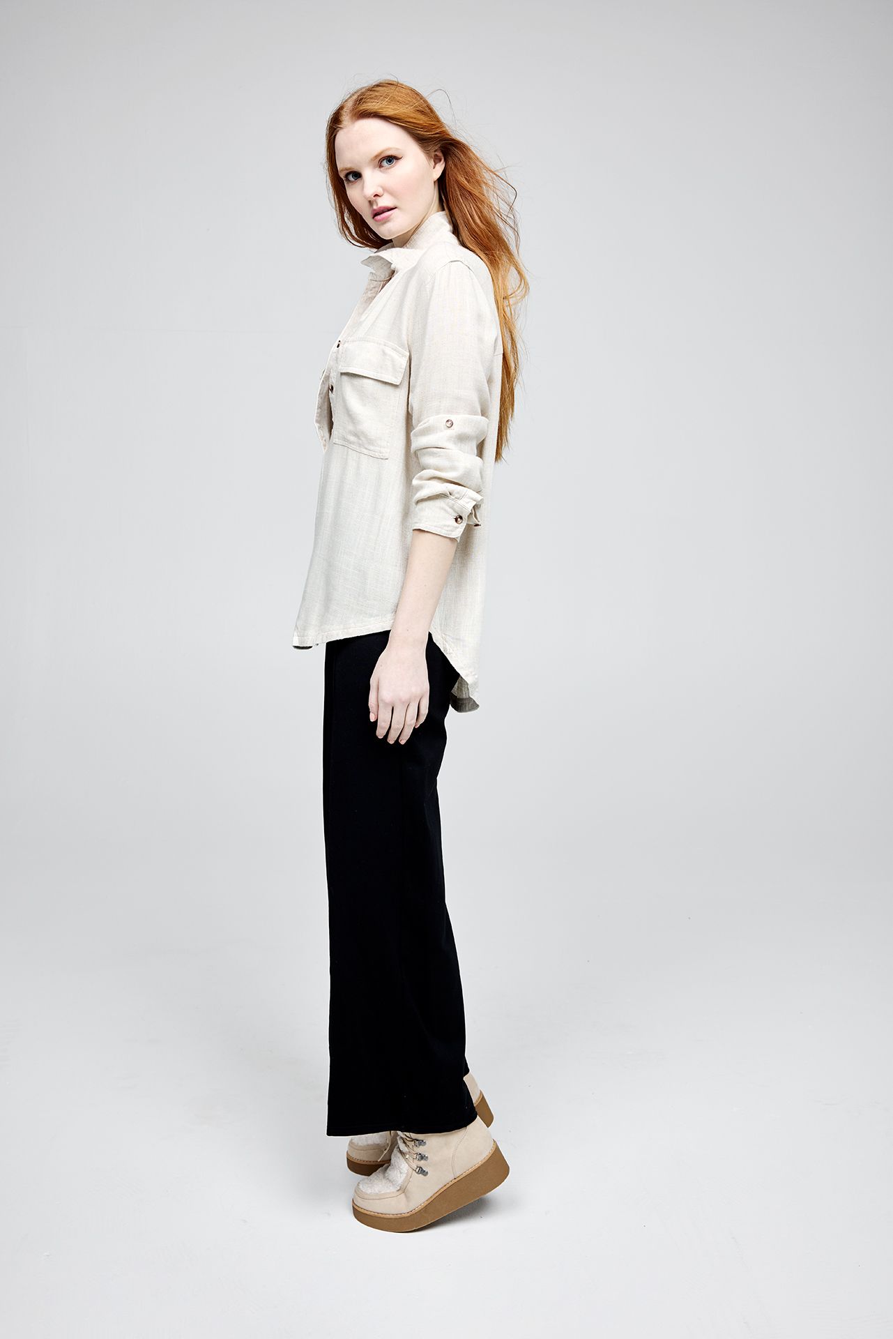 A woman with red hair is wearing a white shirt and black pants.