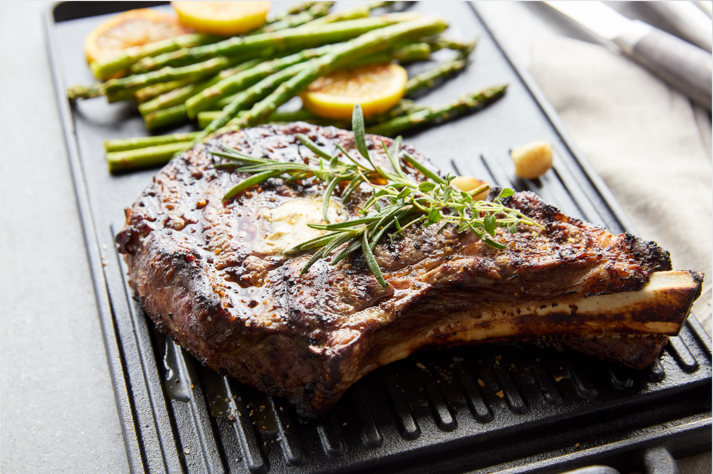 A steak is sitting on a grill next to asparagus and lemons.